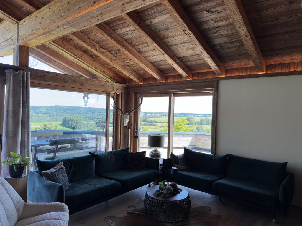 Gemütliches Wohnzimmer mit Holzbalken und großen Fenstern mit malerischem Blick auf die Landschaft.