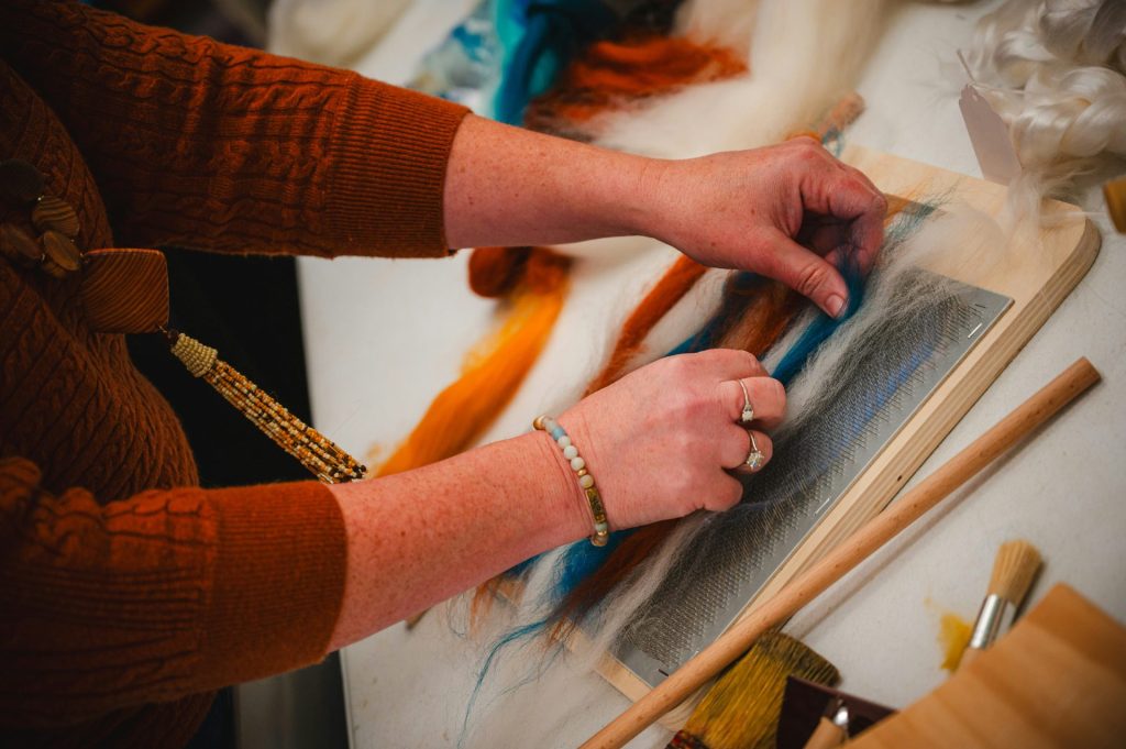 Die Person arbeitet sorgfältig mit bunten Fasern.